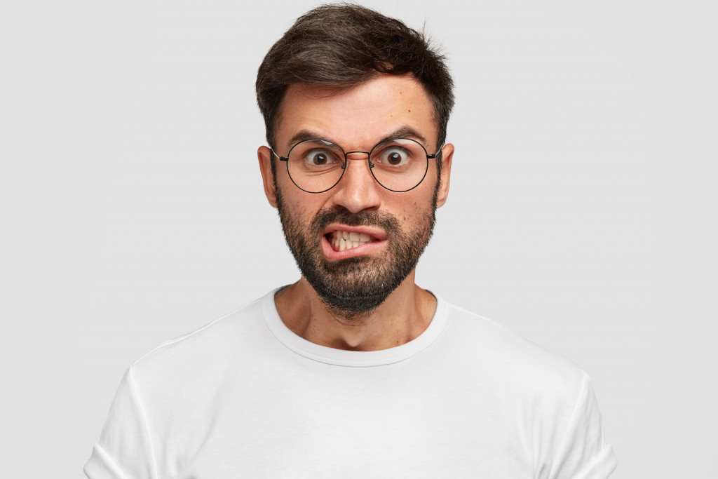 man with eyeglasses clenching his teeth